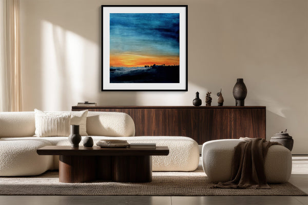 Black-framed abstract sunset print above a dark wood sideboard behind cream seating.