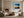 Black-framed abstract sunset print above a low shelf beside a lit stone fireplace.