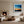 Black-framed abstract sunset print above a low shelf beside a lit stone fireplace.