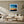 Black-framed abstract sunset print above a cream sofa, wood tables, and a potted tree.