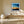 Black-framed abstract sunset print above a long wood bench beside a large ceramic vase.