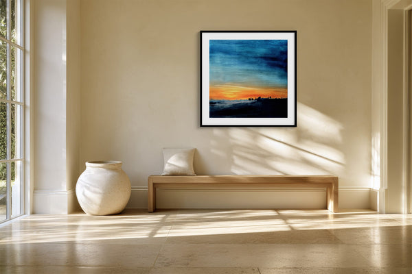 Black-framed abstract sunset print above a long wood bench beside a large ceramic vase.