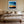 Black-framed abstract sunset print centered above a bed with layered neutral bedding.