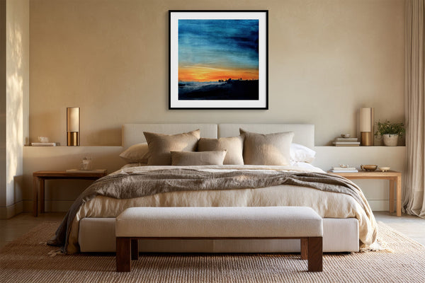 Black-framed abstract sunset print centered above a bed with layered neutral bedding.