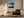 Black-framed abstract sunset print above a dark armchair with a floor lamp and side table.