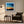 Black-framed abstract sunset print above a dark armchair with a floor lamp and side table.