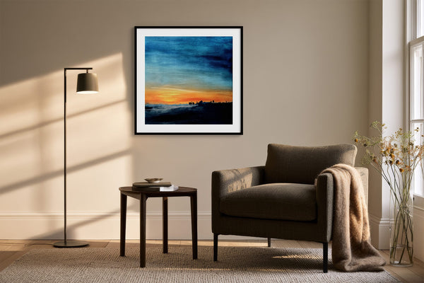 Black-framed abstract sunset print above a dark armchair with a floor lamp and side table.