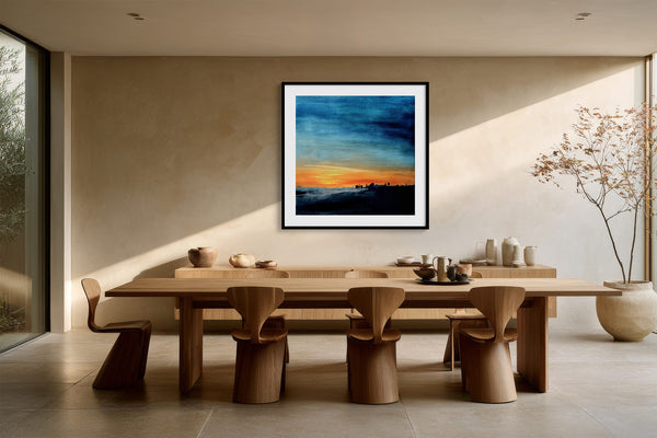 Black-framed abstract sunset print above a long wooden dining table with sculptural chairs.