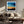 Black-framed abstract sunset print above a cream sofa, wood coffee table, and leafy plants.
