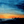 Abstract textured landscape with a vivid orange horizon beneath blue and teal skies and a dark silhouetted ridge.