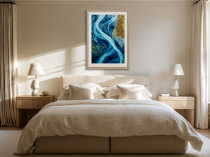 Framed blue glacial river artwork hanging above a bed between matching bedside lamps.