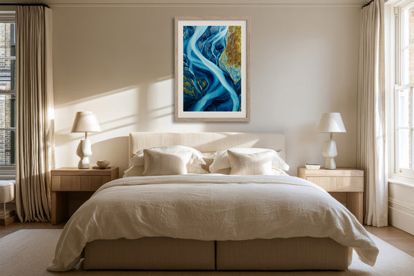 Framed blue glacial river artwork hanging above a bed between matching bedside lamps.