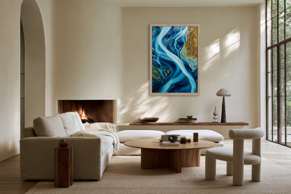 Framed blue glacial river artwork above a fireplace and low seating near tall windows.