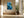 Framed blue glacial river artwork above a built-in bench beside floor-to-ceiling windows and a large vase.