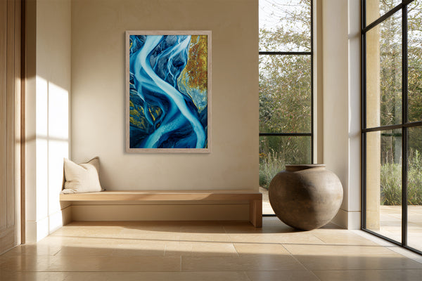 Framed blue glacial river artwork above a built-in bench beside floor-to-ceiling windows and a large vase.