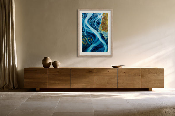 Framed blue glacial river artwork centered above a long wooden sideboard with ceramic vessels.