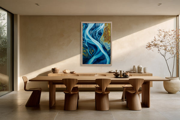 Framed blue glacial river artwork above a long wooden dining table with sculptural chairs.