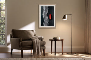 Light-framed shoreline artwork with a red boat displayed above an armchair and side table.