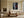 Light-framed aerial shoreline artwork with a red rowing boat above a sofa.