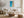 Light wood-framed ocean-and-sand artwork above a cream sofa, rustic table, and woven ottoman.