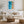 Light wood-framed ocean-and-sand artwork above a cream sofa, rustic table, and woven ottoman.