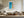 Framed turquoise ocean-and-sand aerial artwork above a cream sectional and wooden coffee table.