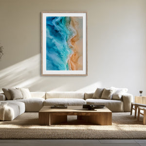 Framed turquoise ocean-and-sand aerial artwork above a cream sectional and wooden coffee table.