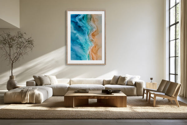 Framed turquoise ocean-and-sand aerial artwork above a cream sectional and wooden coffee table.