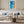 Framed coastal aerial artwork centered above a white sofa with blue-gray cushions.