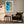 White-framed shoreline artwork above a dark armchair, side table, and floor lamp.