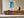 Framed aerial ocean artwork displayed above a long wooden sideboard with a round ceramic vase.