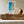 Framed aerial ocean artwork displayed above a long wooden sideboard with a round ceramic vase.