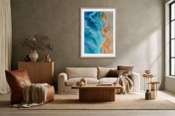 Framed turquoise shoreline artwork above a cream sofa, wooden coffee table, and leather lounge chair.