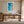 Framed coastal aerial artwork above a wooden desk in a bright workspace with open glass doors.
