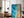 Large black-framed turquoise ocean-and-sand artwork leaning beside a leather armchair and floor lamp.