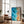 Large black-framed turquoise ocean-and-sand artwork leaning beside a leather armchair and floor lamp.