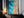 Large thin-framed coastal artwork leaning on a dark wood cabinet beside lit candles.