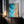 Large thin-framed coastal artwork leaning on a dark wood cabinet beside lit candles.