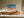 Framed aerial coastal artwork with turquoise waves over orange shore above a wooden sideboard.