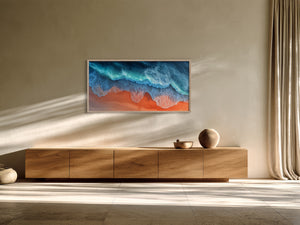 Framed aerial coastal artwork with turquoise waves over orange shore above a wooden sideboard.