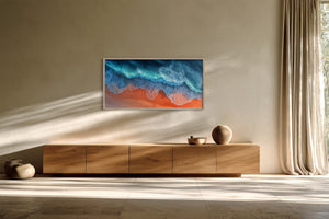 Framed aerial coastal artwork with turquoise waves over orange shore above a wooden sideboard.