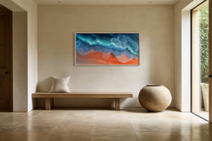 Framed turquoise-wave and orange-shore artwork above a wooden bench beside a large ceramic vessel.
