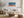 Light wood-framed coastal artwork above a white sofa with pillows and a round wooden coffee table.