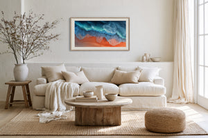 Light wood-framed coastal artwork above a white sofa with pillows and a round wooden coffee table.