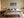 White-framed turquoise and orange coastal artwork centered above a bed with neutral bedding.