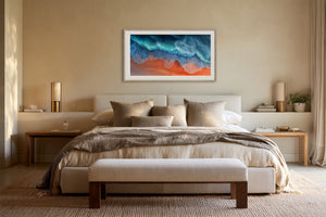 White-framed turquoise and orange coastal artwork centered above a bed with neutral bedding.