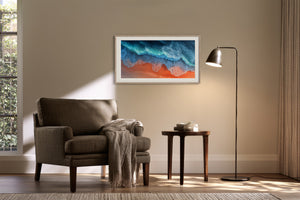 White-framed aerial coastal artwork above a dark upholstered armchair and side table.