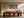 Large framed turquoise-wave and orange-shore artwork above a long wooden dining table.