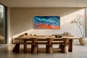 Large framed turquoise-wave and orange-shore artwork above a long wooden dining table.