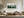 Misty pine forest watercolor in a light wood frame above a cream sectional sofa.